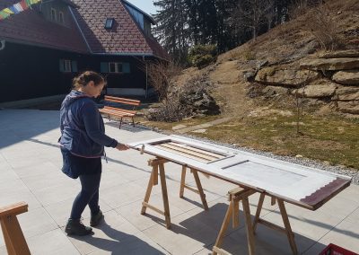 A female volunteer paints a white door outdoors during KALAPA CARE, the volunteer week at Kalapa Retreat Center.
